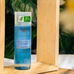 Eucerin DermatoCLEAN Hyaluron toner bottle surrounded by wooden frame and plants.
