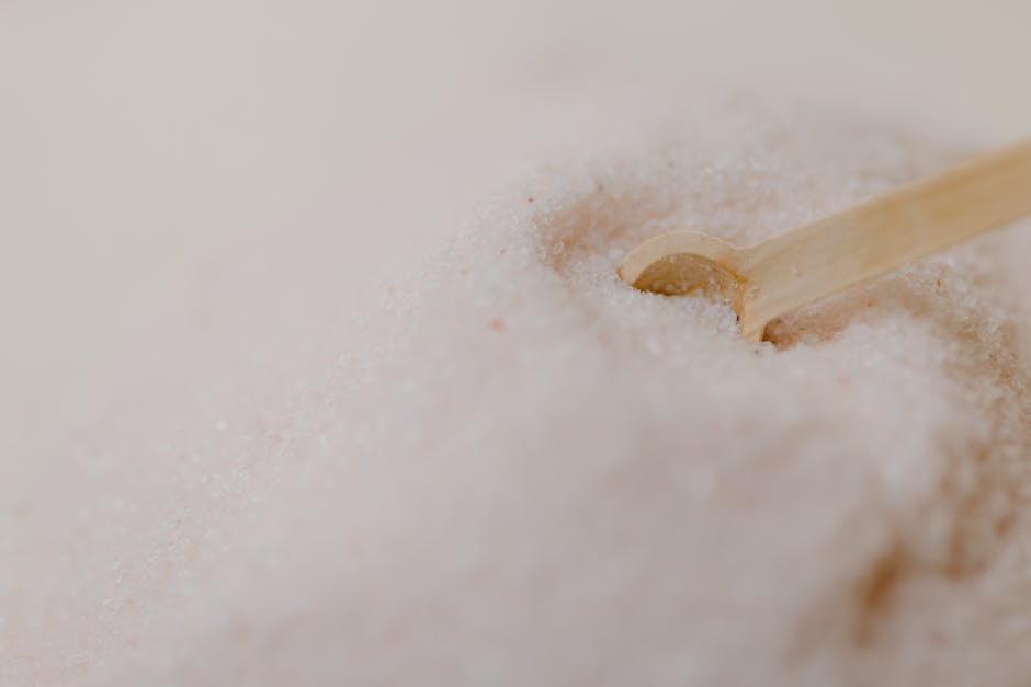 A detailed close-up of pink Himalayan salt with a wooden spoon on a smooth surface.