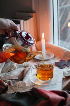 Warm and inviting scene of tea being poured from a kettle, with candlelight and autumn leaves creating a cozy atmosphere.