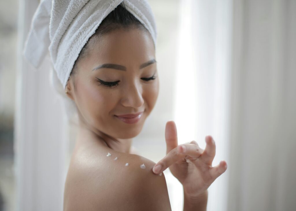 Elegant portrait of a woman applying skincare cream indoors, highlighting beauty and relaxation.
