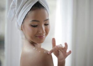 Elegant portrait of a woman applying skincare cream indoors, highlighting beauty and relaxation.