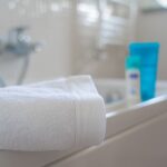 A neatly folded white bath towel on a bathtub edge with blurred bath products in the background.